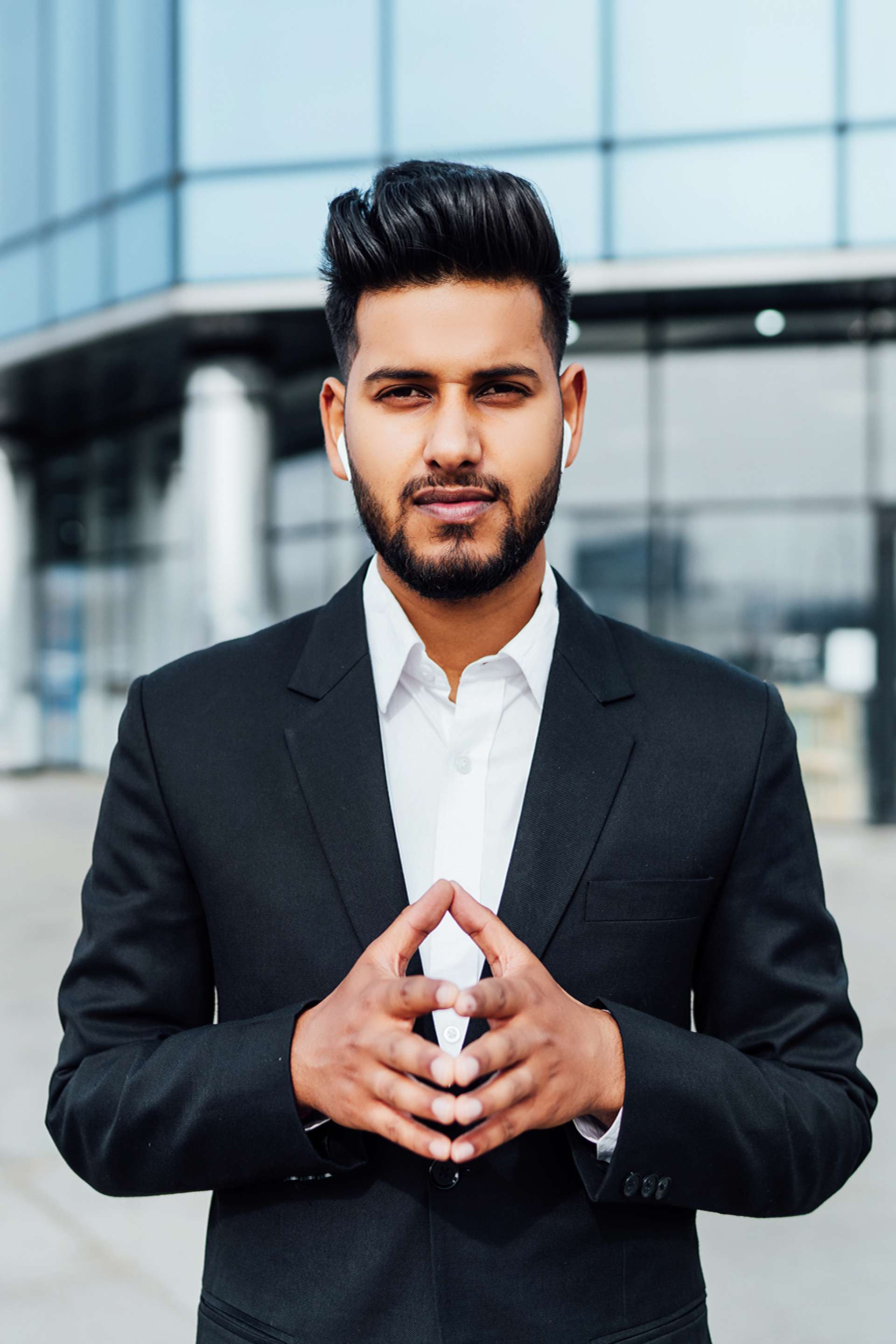 portrait-serious-smiling-modern-indian-man-near-office-building Portrait of a serious smiling modern Indian man, businessman, in front of the holding, behind him a modern building, he is looking at the camera.